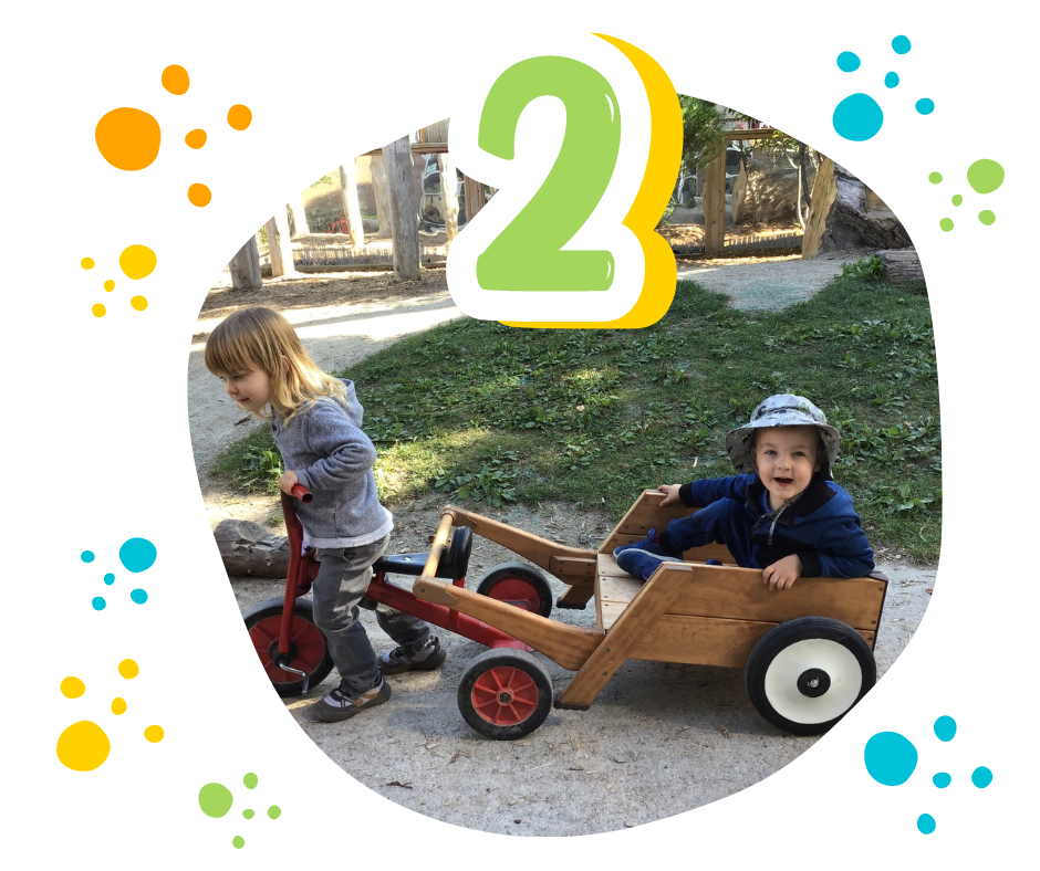 child riding a tricycle that tows a wagon carying another child