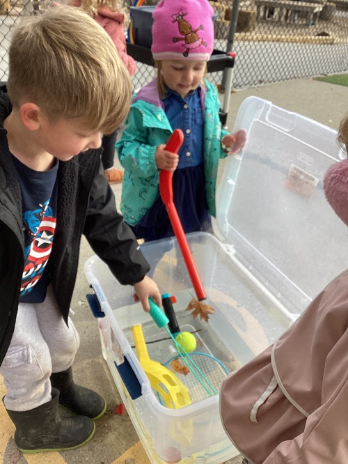 children experiementing with what items sink or float in a bucket of water