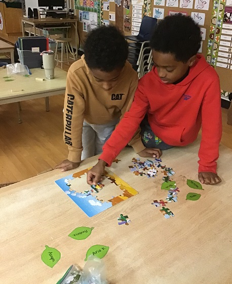 two children standing at a table working on a puzzle