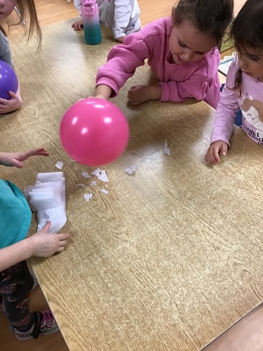 Children using a balloon to pick up small pieces of paper due to static electricity
