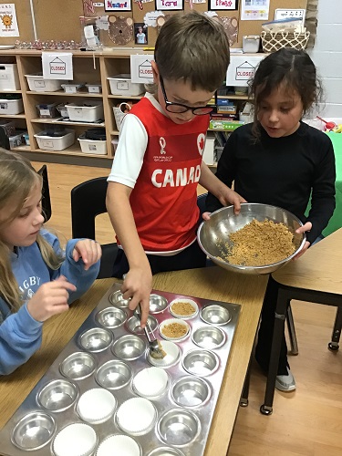 Three children filling muffin tins with crushed graham crackers