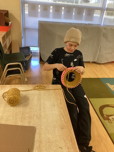 School-age boy working hard on his knit loom