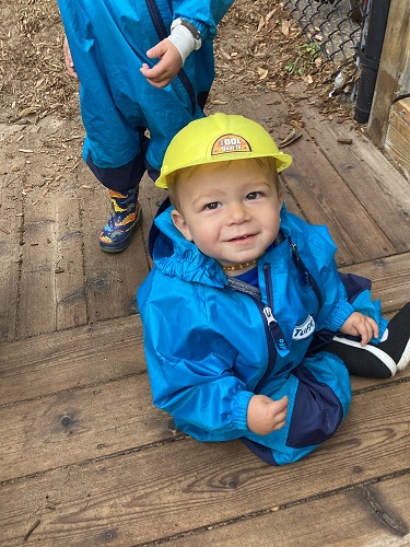 A child sitting outside wearing a plastic fire fighter hat