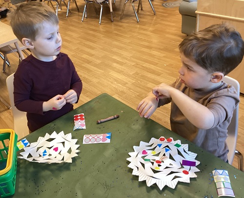 Two children putting stickers on paper snowflakes