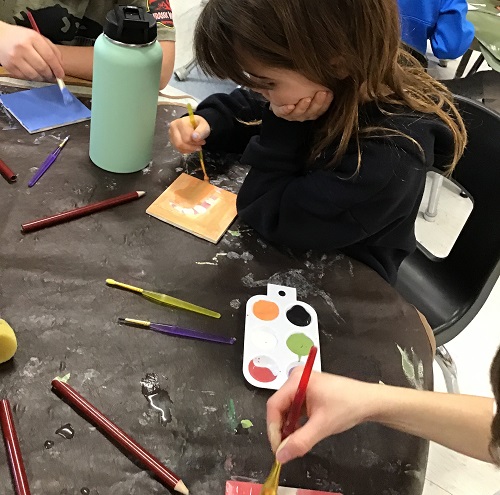 A child painting a tile at the table