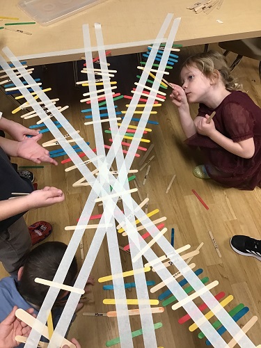 Children sticking popsicle sticks to tape to create a bridge