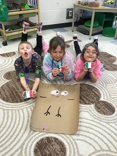 Three children laying on the floor in front of their team mascot they created