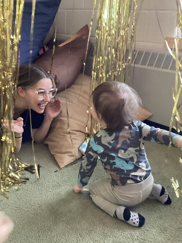 An educator and child playing peek a boo in the tinsel