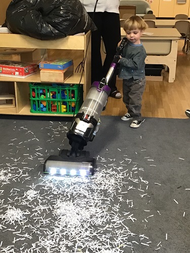 A child using a vacuum on the carpet in the classroom