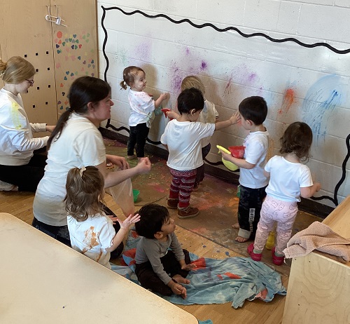 Educators and a group of children using chalk powder to colour the walls and each other's shirts