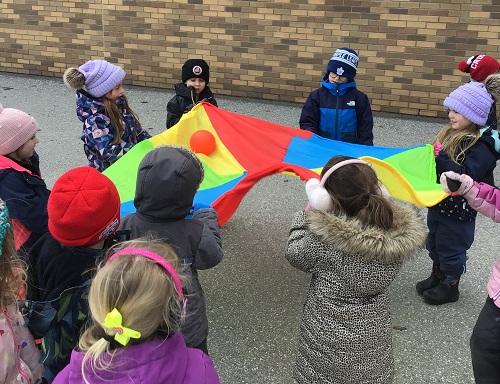 Children surrounding a parachute with a ball in the middle