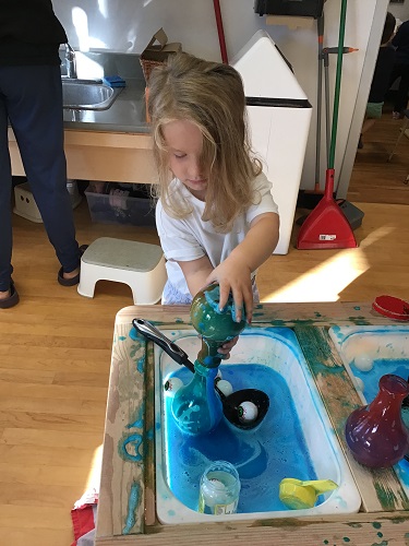 Preschool child holding a potion bottle with blue liquid inside over top of another potion bottle and looking at the to potion bottles