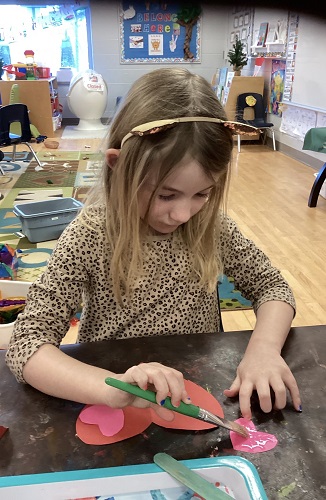 A child spreading glue onto a paper heart