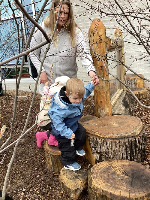 Toddler children climbing on the logs with an educator