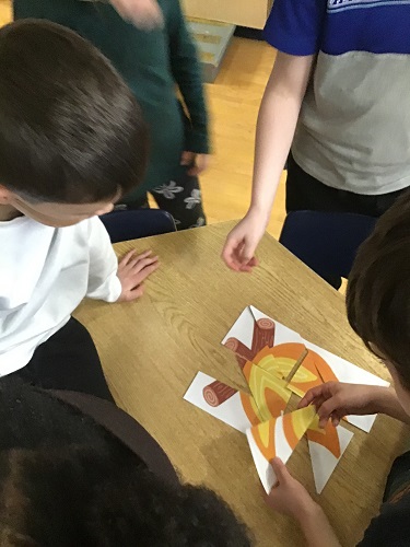 5 school age children gathered around a table putting together puzzle pieces of a camp fire