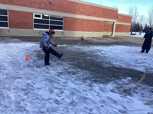 school-age girl kicking soccer ball