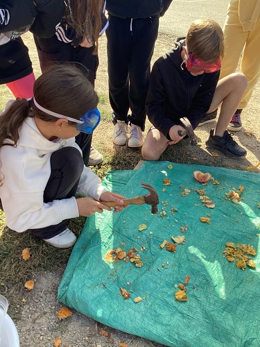 2 School-age children using hammers to break gourds