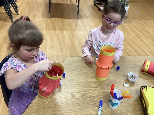 2 school age children sitting at a table creating paper lanterns