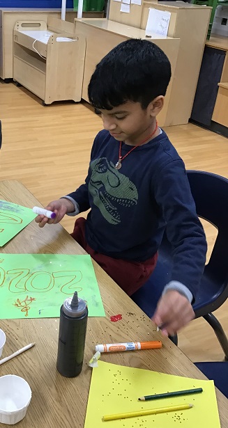 A school age child sitting at a table using markers to create a 2026 poster