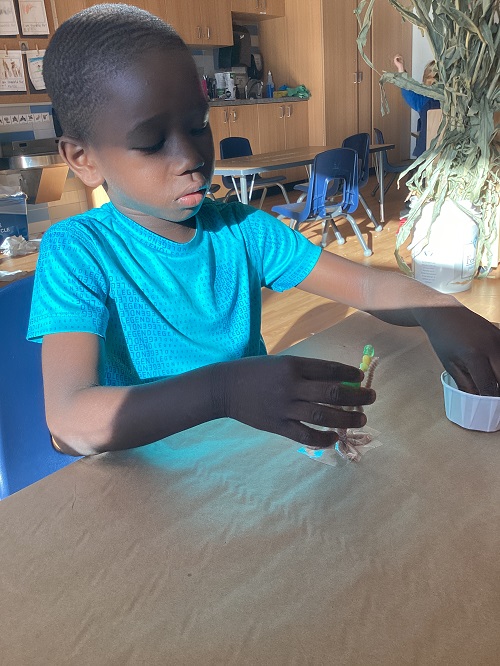 A school age child using their fine motor skills to place beads on a pipe cleaner tree
