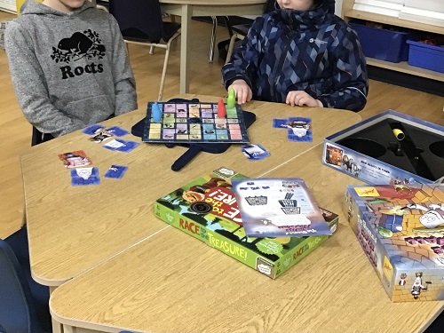 2 School Age children sitting at a table with a board game in front of them, they are looking at the board game