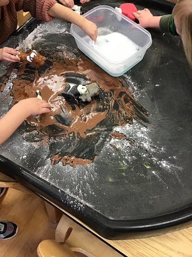 Brown mud on the tuff tray with animals in the mud and a bucket of soap and water on the tuff tray on the side