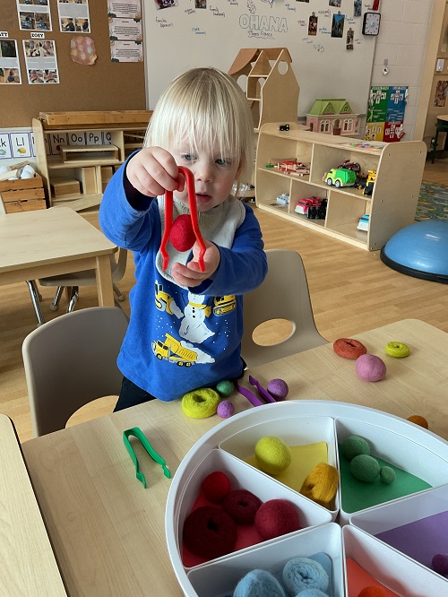 child with tongs and pom poms