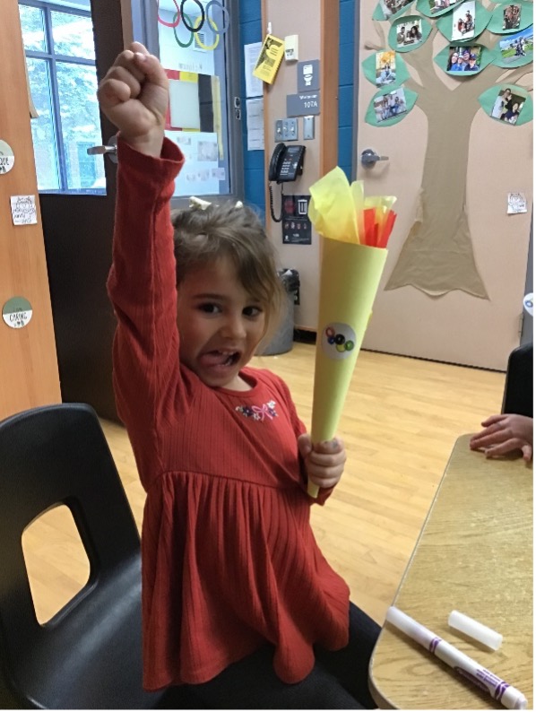 Child holding a craft project of the olympic flame in a classroom