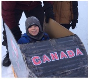 Child in a cardboard bobsled outside in winter