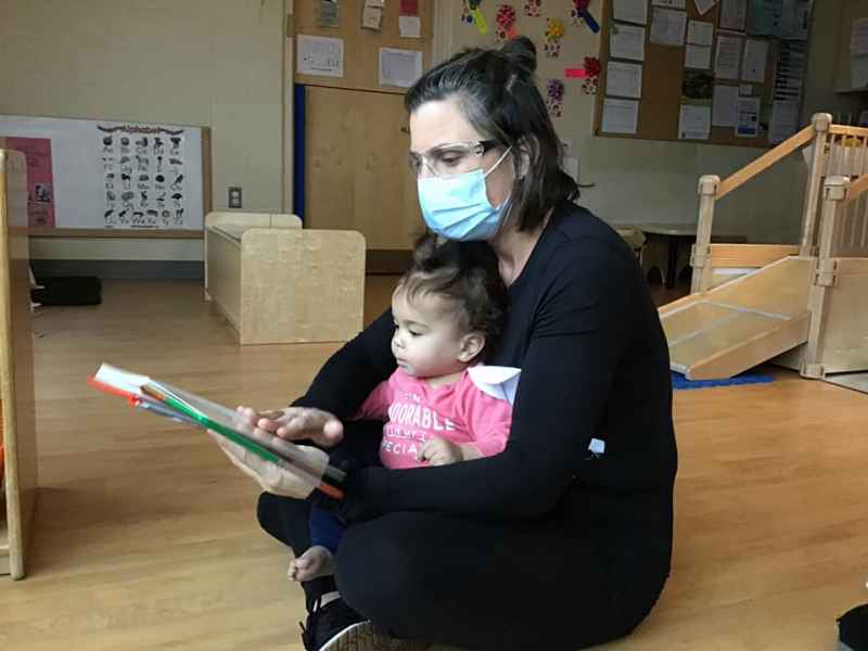 educator reading a book to an infant sitting on her lap