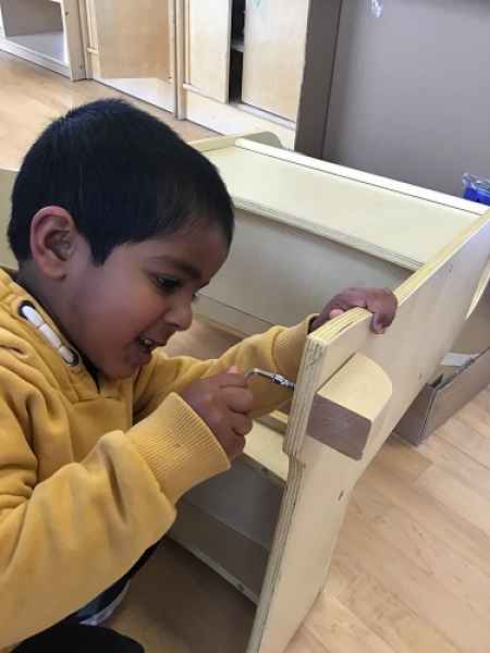 boy using tools to put a screw in a stool
