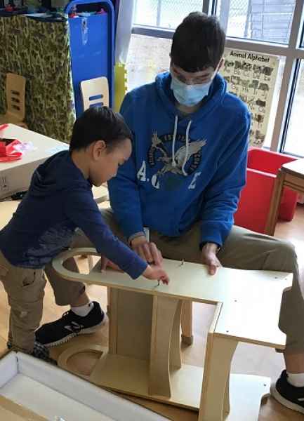 educator helping boy put screws in a wooden stool