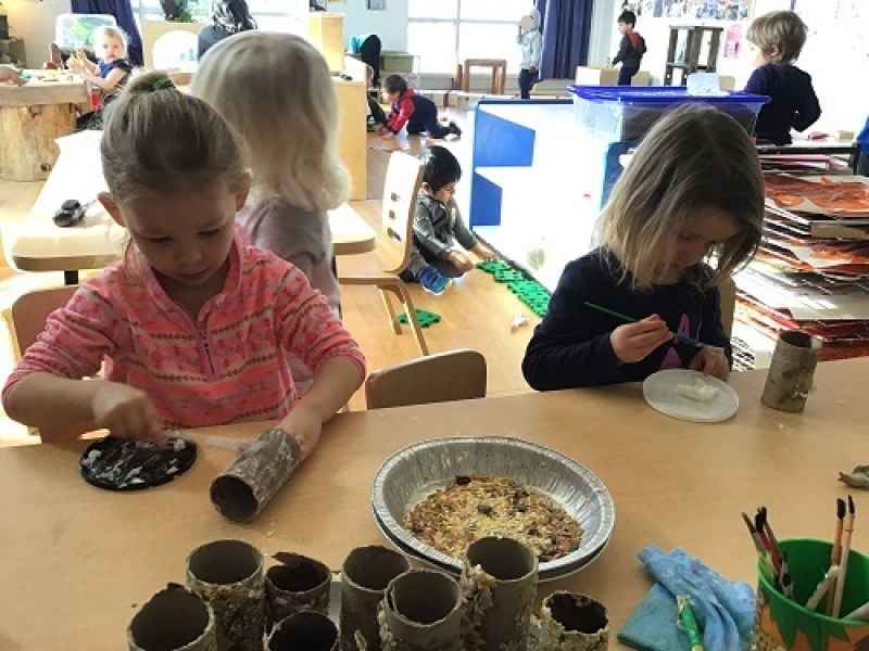 girls sitting at a table gluing birdseed to paper