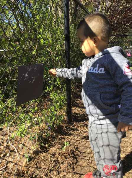 boy painting on a paper hung on the fence
