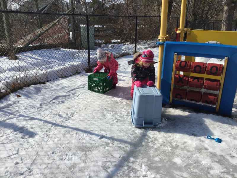 children pushing a bin across the ice outside in their playground