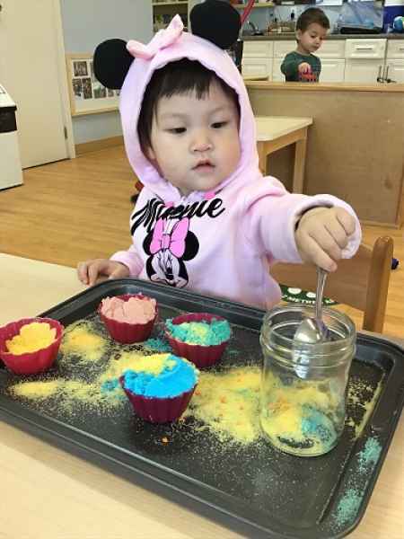girl mixing coloured sand in a sensory bin