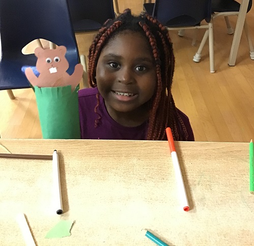 child at a desk with a pupper made of paper