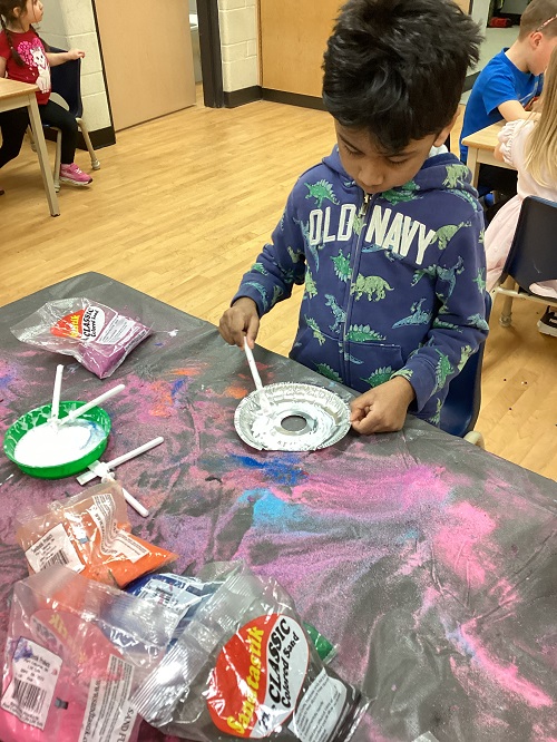 child applying glue to an aluminum canvas for sand art