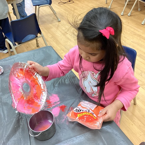 child dumping colourful sand into a small bucket