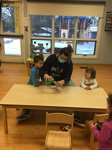 A toddler educator is pouring Sprite into a bottle with some toddler children.