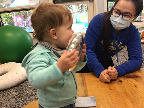 child holding a reflective toy as educator smiles at them