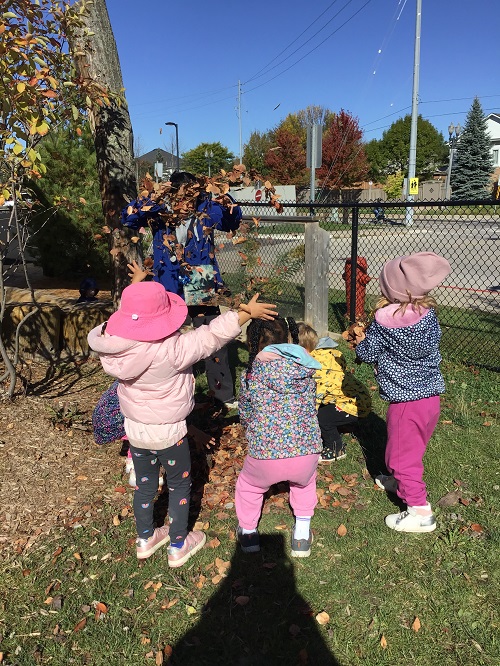Children throwing leaves in the air with their educator. 