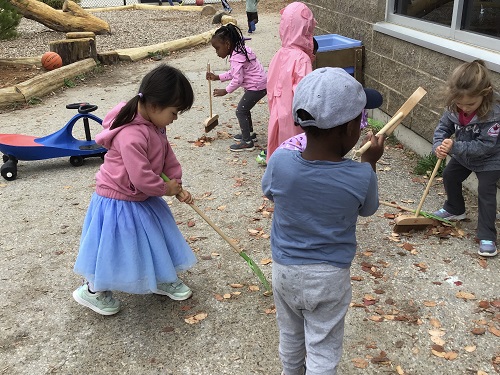 Children sweeping leaves on the playground. 