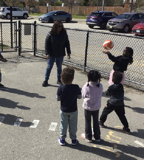 Children in a circle playing volley ball outside.