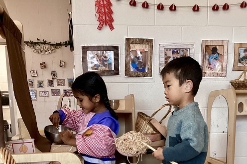 2 preschool children engaged in pretend play with noodles and bowls
