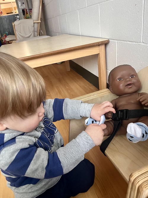 An infant child putting socks on a toy baby