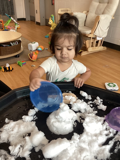 An infant child playing with snow in the tuff tray