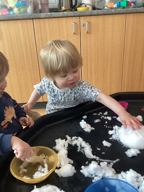 An infant child playing with snow in the tuff tray