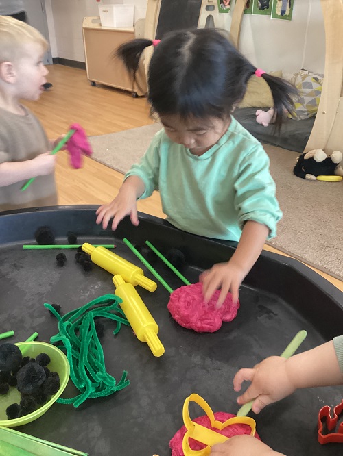 A toddler using playdough on a tuff tray