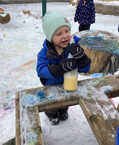 A child happily exploring with a spray bottle filled with coloured water.